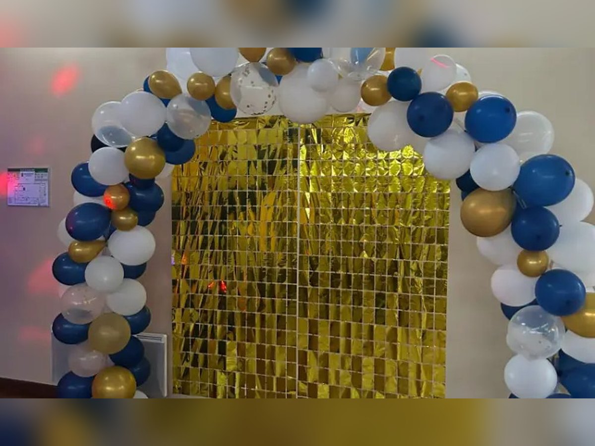 Arche de ballons bleus, blancs et argentés montée devant un rideau argenté dans une salle de réception