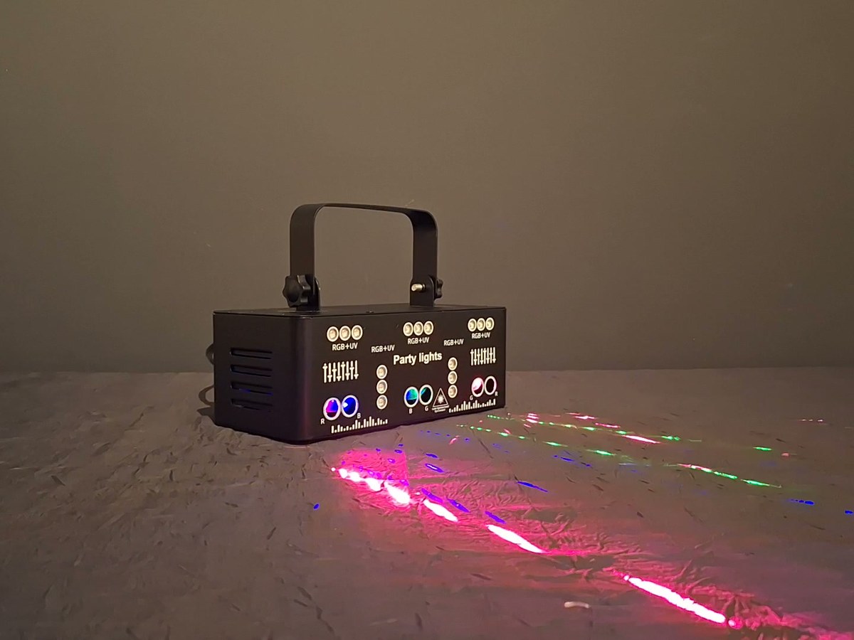 Projecteur laser posé au sol, faisceaux rouges et verts filant vers la droite