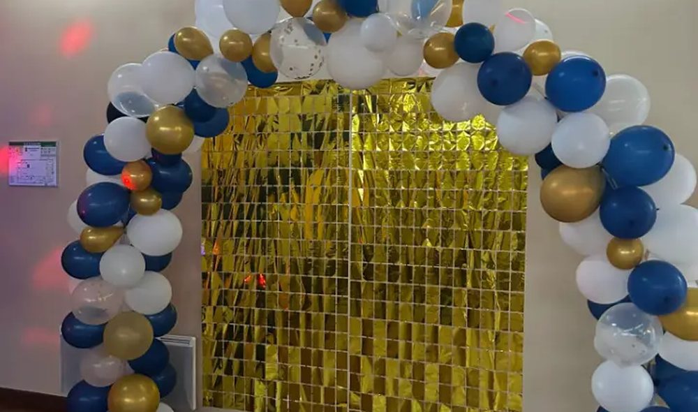 Arche de ballons bleus, blancs et argentés montée devant un rideau argenté dans une salle de réception